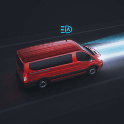 Red Ford Transit at night with headlights on. The headlight-on indicator is seen.