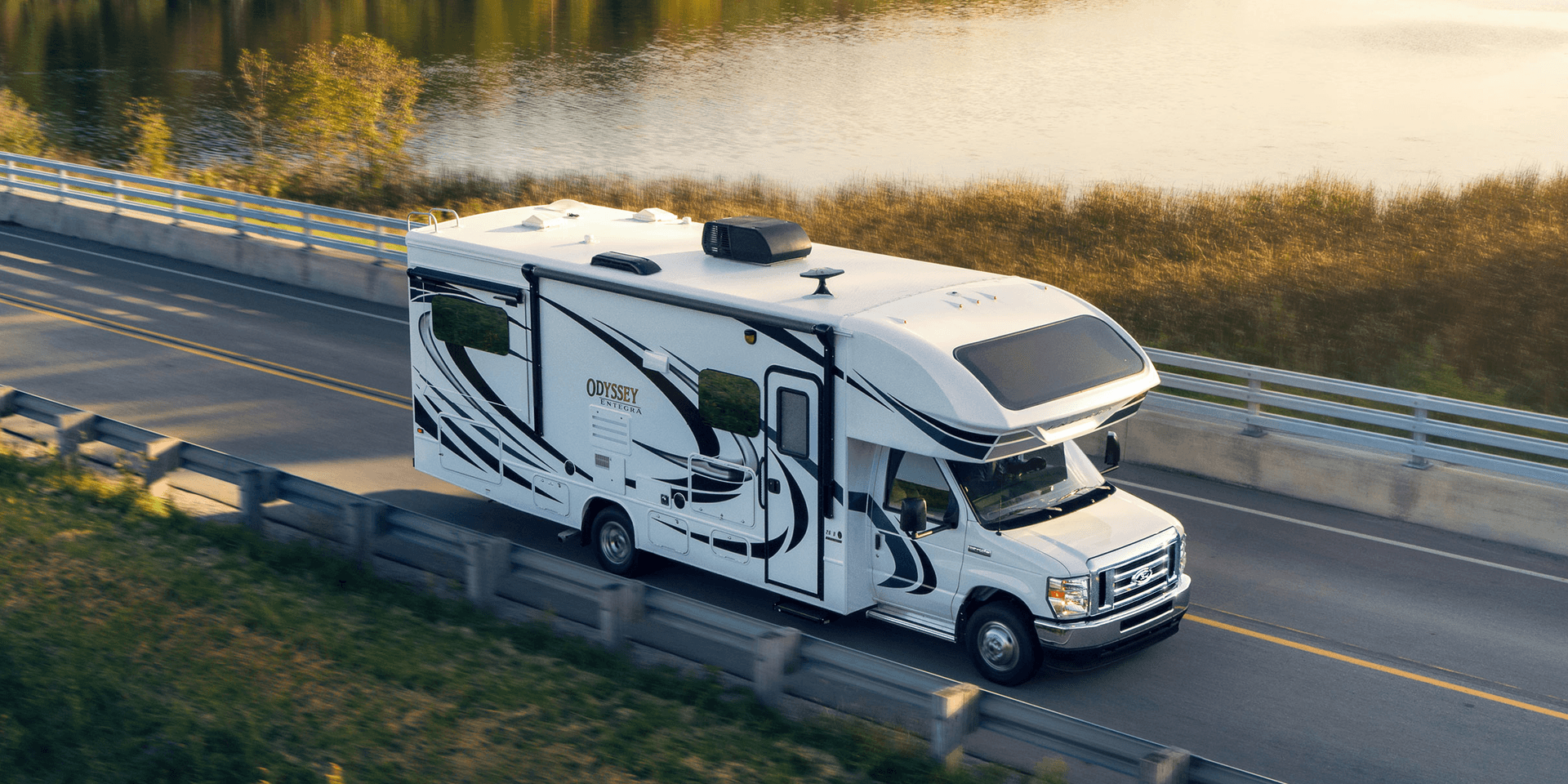 A Class C motorhome is driving past a body of water.